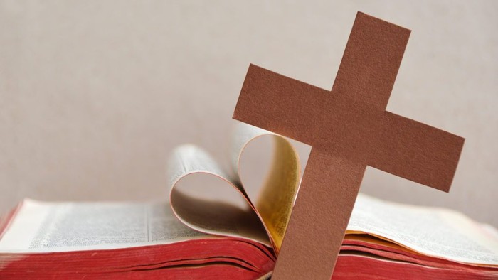 Ein braunes Kreuz liegt auf einem aufgeschlagenen Buch mit roter Markierung.