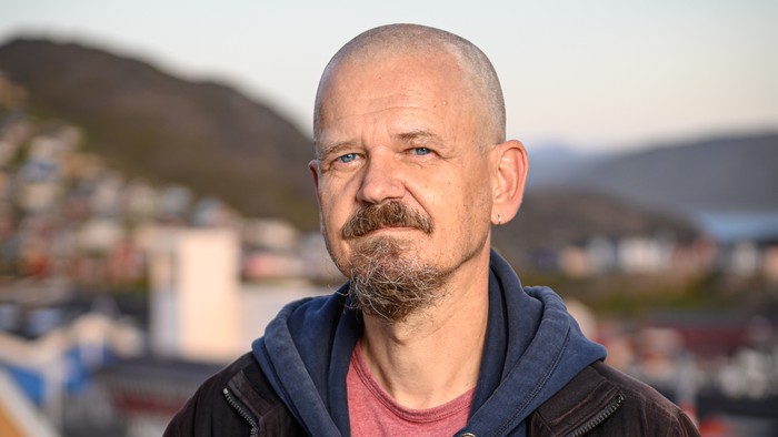 En bald, bart mands ansigt, tørretøj og en by i baggrunden