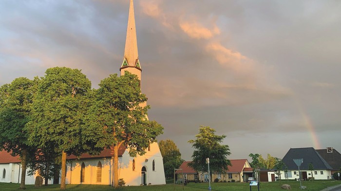 Kirche mit hohem Turm, Regenbogen am Himmel, umgebende Häuser