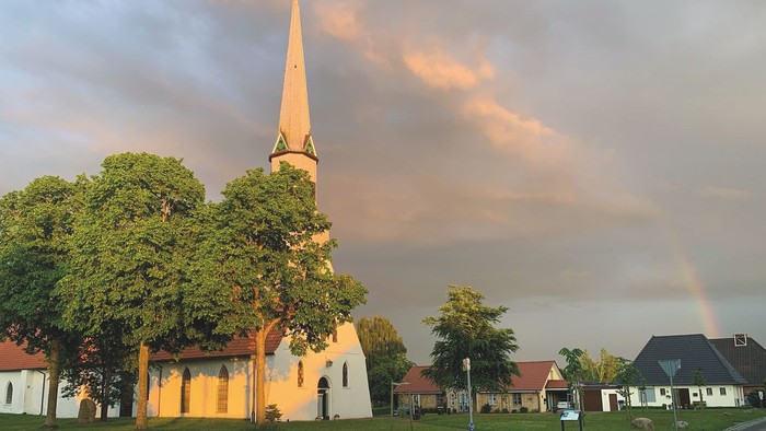 Kirche mit hohem Turm, Regenbogen am Himmel, umgebende Häuser