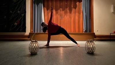 Person, die Yoga in der Dreieckshaltung praktiziert, mit dekorativen Lampen und festlichen Luftballons im Hintergrund.