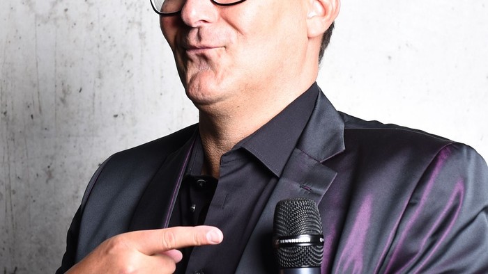 Mann in Anzug hält Mikrofon und zeigt mit Finger