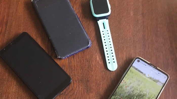 Smartphone, Fitness-Tracker und zwei Handyhüllen auf einer Holzoberfläche angeordnet.