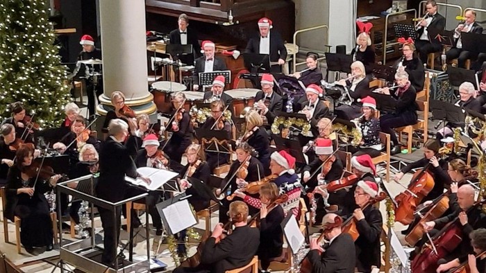 Orchestra performing on stage with conductor and musicians playing various instruments.