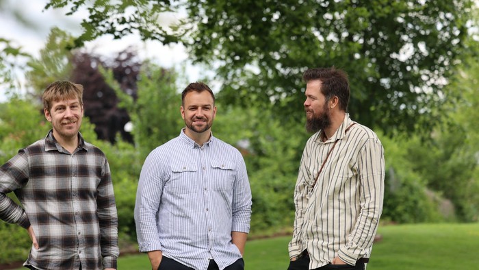 Tre mænd står sammen i en have.