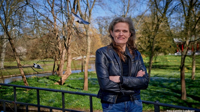 Kvinde i blå jacke står med armene krydsede ved en bro over en kanal.