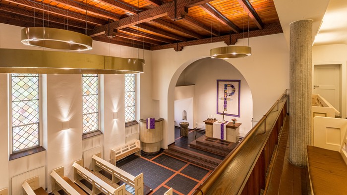 Das Bild zeigt einen großen Raum mit Holzbalkendecke, einem Treppenhaus und einem großen "P"-Wanddekoration.