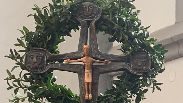 Ein Kreuz mit Jesusfigur und grünem Kranz an der Wand