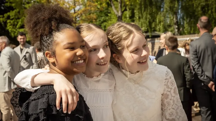 Tre glade unge piger i formelt tøj, der poserer sammen udendørs til en begivenhed.