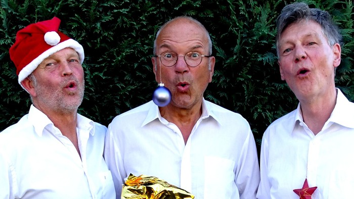 Drei Männer in weißen Hemden singen Weihnachtslieder und halten goldene Geschenkpapier.