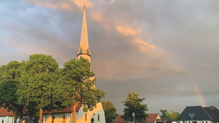 Kirche mit hohem Turm, Regenbogen am Himmel, umgebende Häuser
