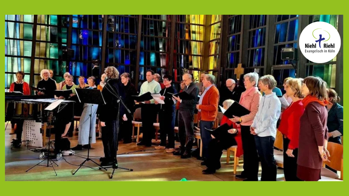 Ein Chor probt in einem großen Raum mit hohen Fenstern und Beleuchtung.