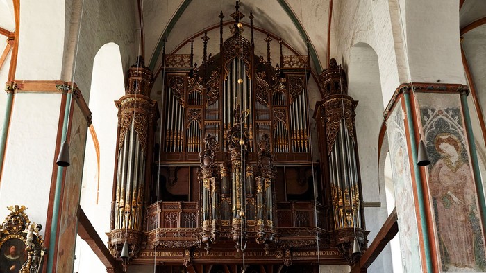 Historisches Kircheninneres mit einem prunkvollen Pfeifenorgel und hölzernen Kirchenbänken unter einem Gewölbe.