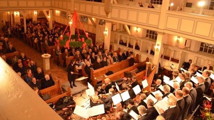Großer Saal mit vielen Menschen, Chor singt, Zuschauer auf Balkonen