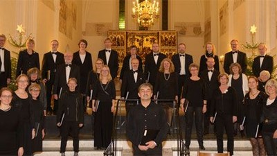 En stor korgruppe i formel klædning optræder i en prægtig sal.