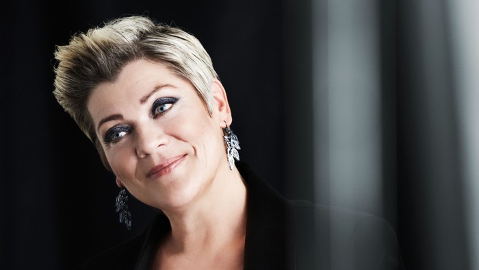 En kvinde med kort hår og sort klæde ler til kameraet.