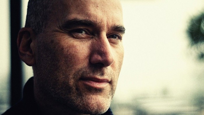 Skaldet mand med skæg, der smiler blidt, iført mørkt tøj.