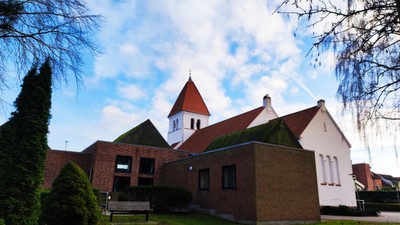 En kirke med røde tag og en klokketårn modsat et blåt himmel.