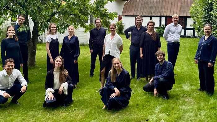 Gruppe af mennesker klædt i koordineret mørkt tøj, der poser udendørs i en have.