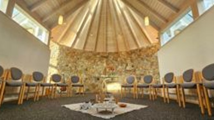 Ein ruhiger Raum mit Stühlen und einem Tisch in der Mitte, umgeben von Fenstern und einer Steinsäule.