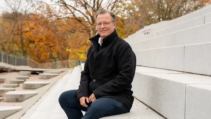 Mand sidder på trappe i sort jakke og blå briller.