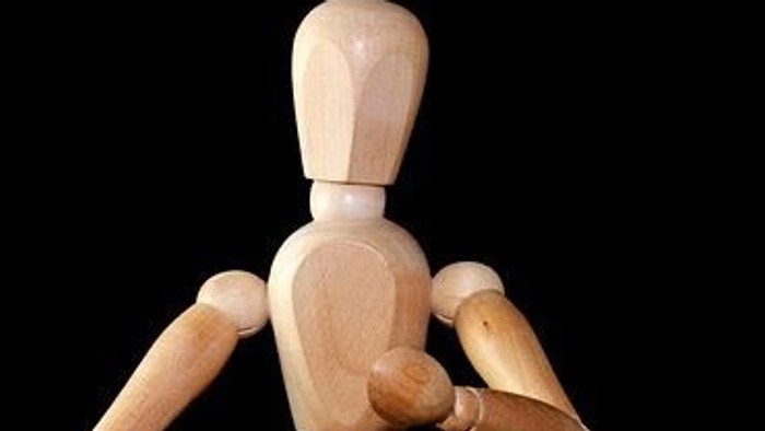 Holzfigur mit verschränkten Armen vor schwarzem Hintergrund