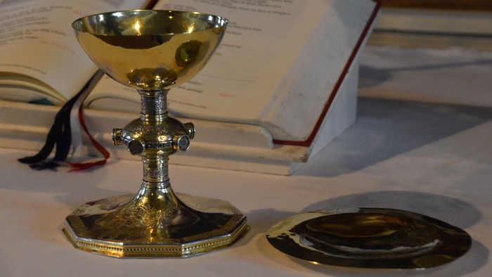Ein goldener Kelch und eine Patene auf einem Tisch neben einem geöffneten religiösen Buch.