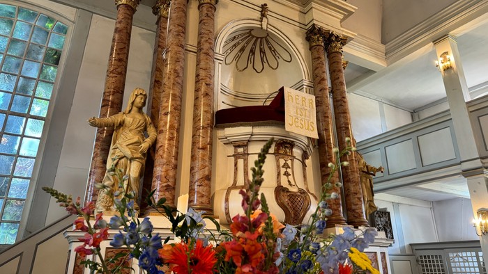 Eleganter Altar, geschmückt mit Statuen, verzierten Säulen und üppigen Blumenarrangements in einem prächtigen Kircheninnenraum.