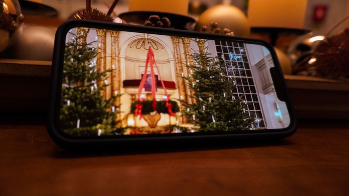 Ein Smartphone, das eine festliche Weihnachtsbaum-Szene mit Feiertagsdekorationen und Lichtern anzeigt.