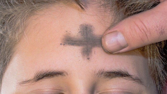 Eine Hand zeichnet ein Aschenkreuz auf die Stirn einer Person