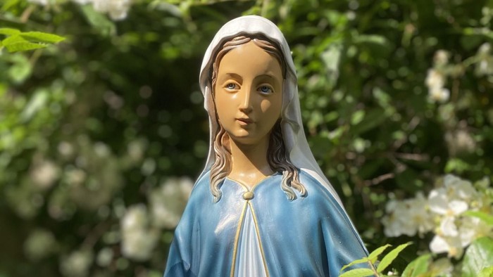 Die Statue einer Frau in Blauem Kleid vor grünem Blattwerk