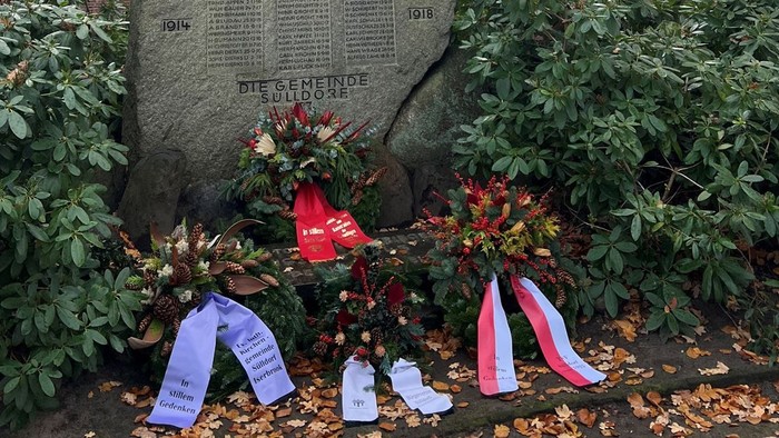 Blumengebinde und Bänder vor Gedenkstein