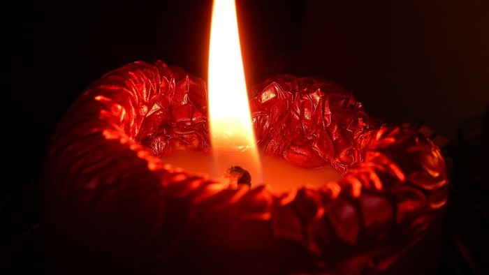 Eine rote Kerze brennt im Dunkeln.