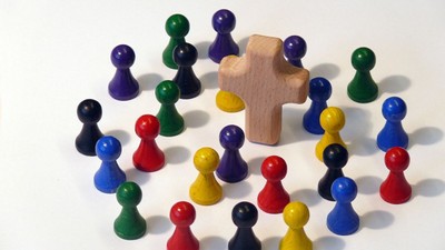 Holzfiguren in verschiedenen Farben um ein hölzernes Kreuz angeordnet