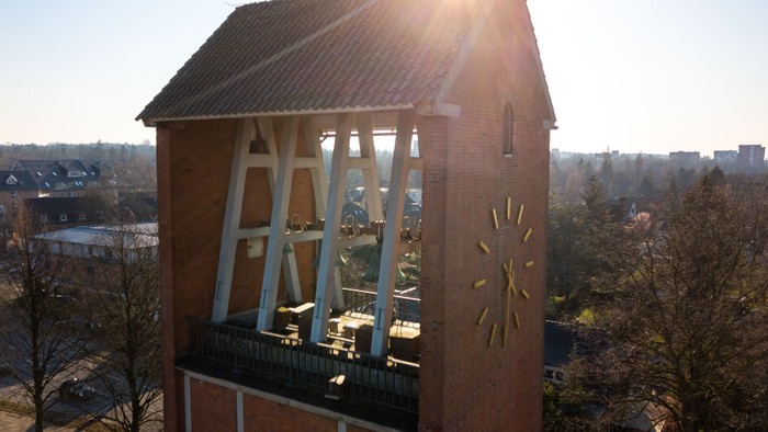 Ein hoher Ziegelbau mit Uhr und Sonnenuhr, umgeben von Bäumen und Häusern