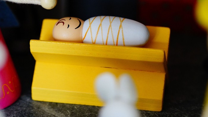 Eine kleine hölzerne Krippe mit einer Babyfigur darin, in Windeln gewickelt.