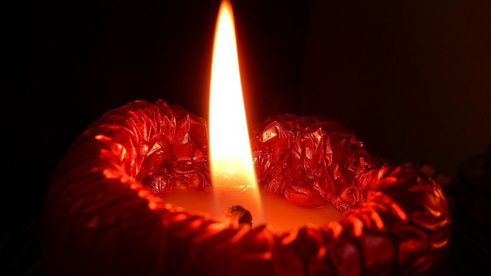 Eine rote Kerze brennt im Dunkeln.