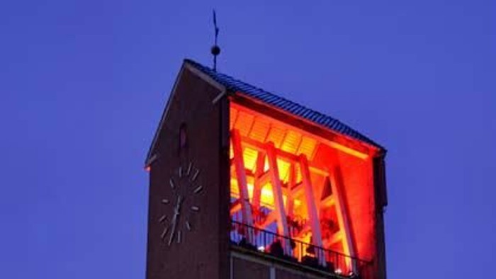 Ein hoher Ziegelturm mit beleuchtetem Uhrwerk bei Dämmerung