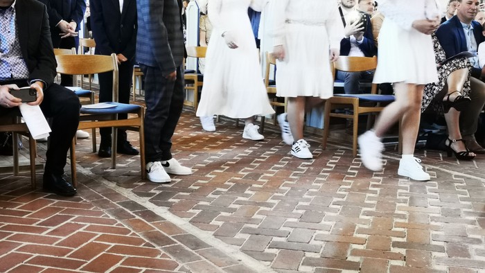 En gruppe af mennesker står i en hal med murstenet gulv og diskuterer.