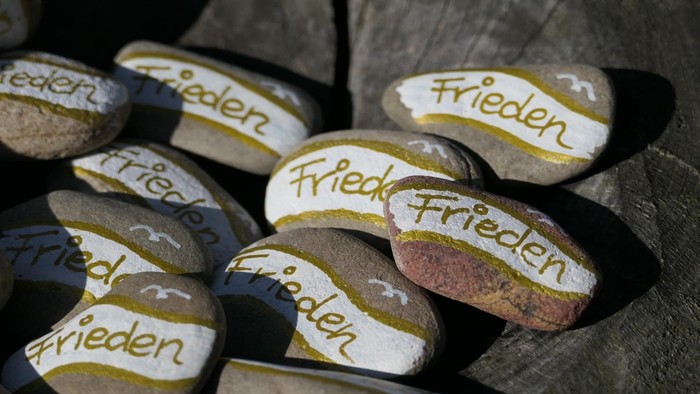 Steine mit der Aufschrift "Frieden" liegen auf einem Baumstamm