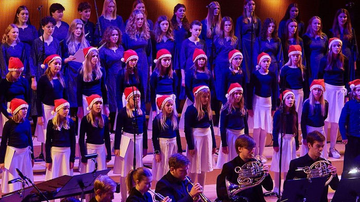 Stort kor, der optræder på scenen med instrumentalister foran.