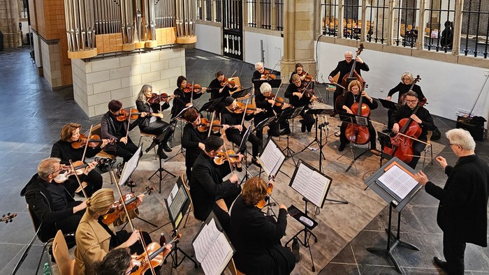 Ein Orchester spielt in einer prächtigen Kathedrale mit hohen Gewölben und bunten Glasfenstern.