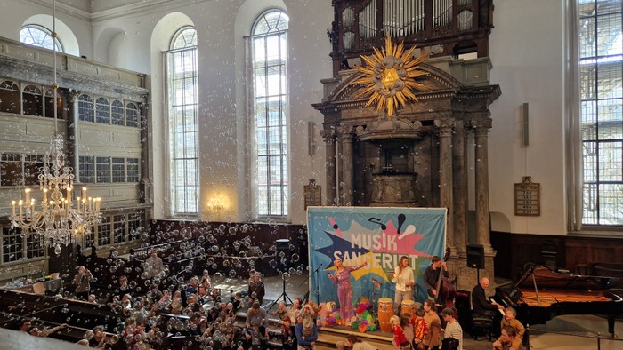 En stor koncerthal med publikum og orkester på scene foran et orgel.