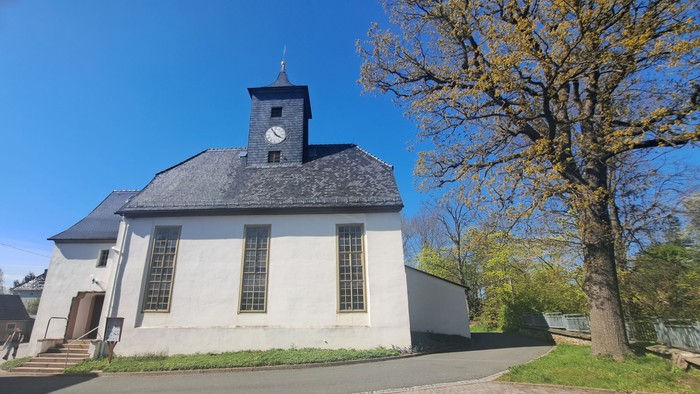 Weißes Kirchlein mit Uhrturm unter blauem Himmel