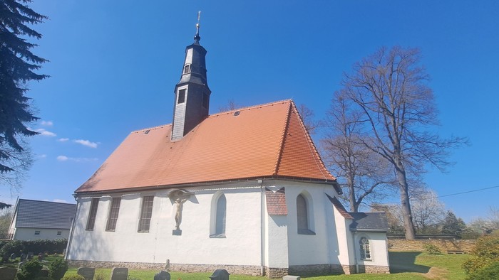 Kleine weiße Kirche mit rotem Dach und hohem Turm unter blauem Himmel