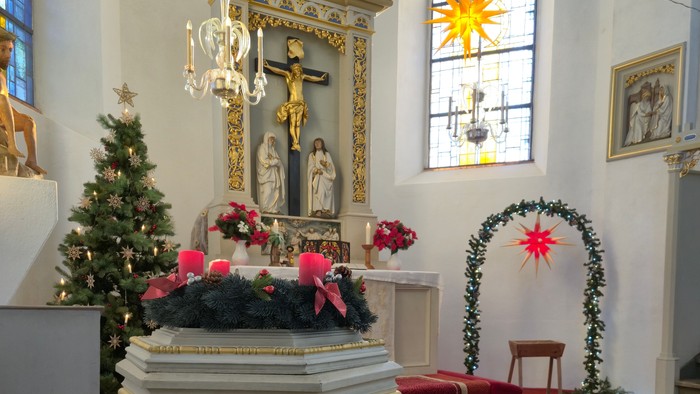 Elegante Kircheninnenausstattung mit festlichen Dekorationen, darunter ein Taufbecken, ein Altar und Weihnachtsbäume.