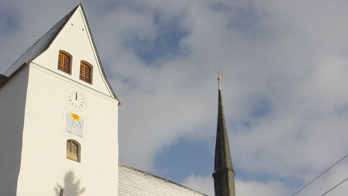 Weiße Kirche mit hohem Turm und schneebedeckten Büschen davor
