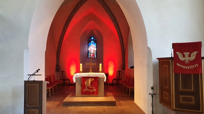 Kircheninneres mit rotem Buntglas, Altar und hölzerner Ausstattung