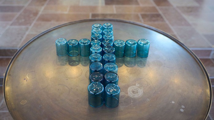 Et rundt bord bærer en korsformet opstilling af blå lys i en rolig indendørs kapelscene.