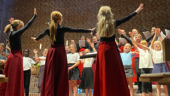 En gruppe kvinder i røde skørter og sorte topper danser på en scene foran en publikum.